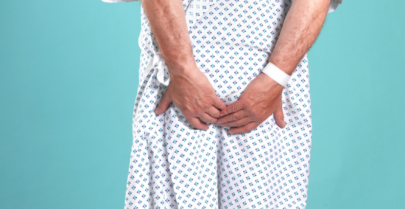 Rear view of man in hospital gown, clutching buttocks