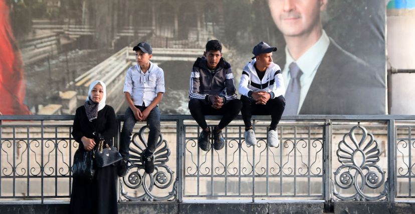 عائلات سورية تنتظر أمام صورة الأسد